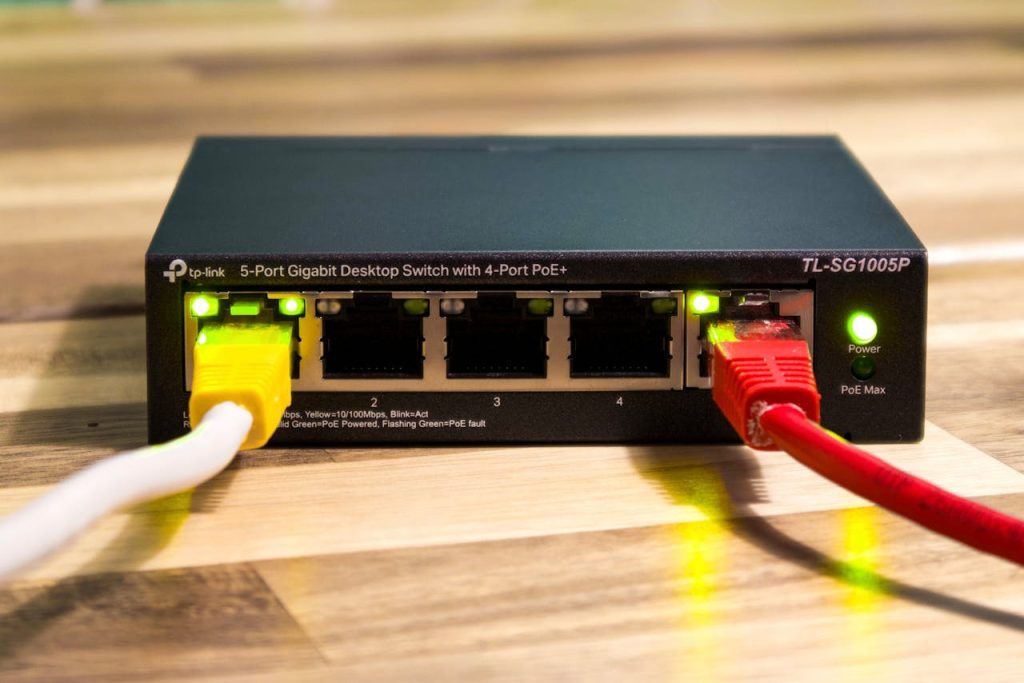 ethernet-switch-with-connected-cables-on-wooden-surface-32698413 Close-up of a TP-Link Ethernet switch with yellow, red, and white cables connected.